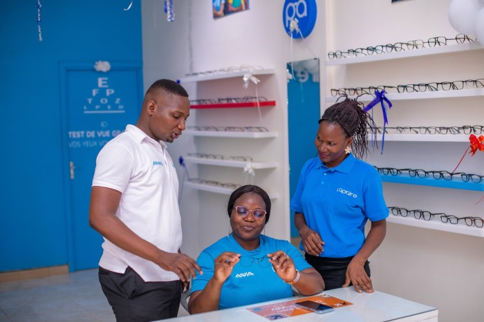 Three people, who appear to be employees of an optical shop, examine eyeglasses